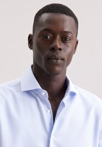 Lichtblauw gestreept shirt met witte knopen, puntige kraag en een getailleerd ontwerp. Glad stoffen textuur, met smalle verticale lijnen.