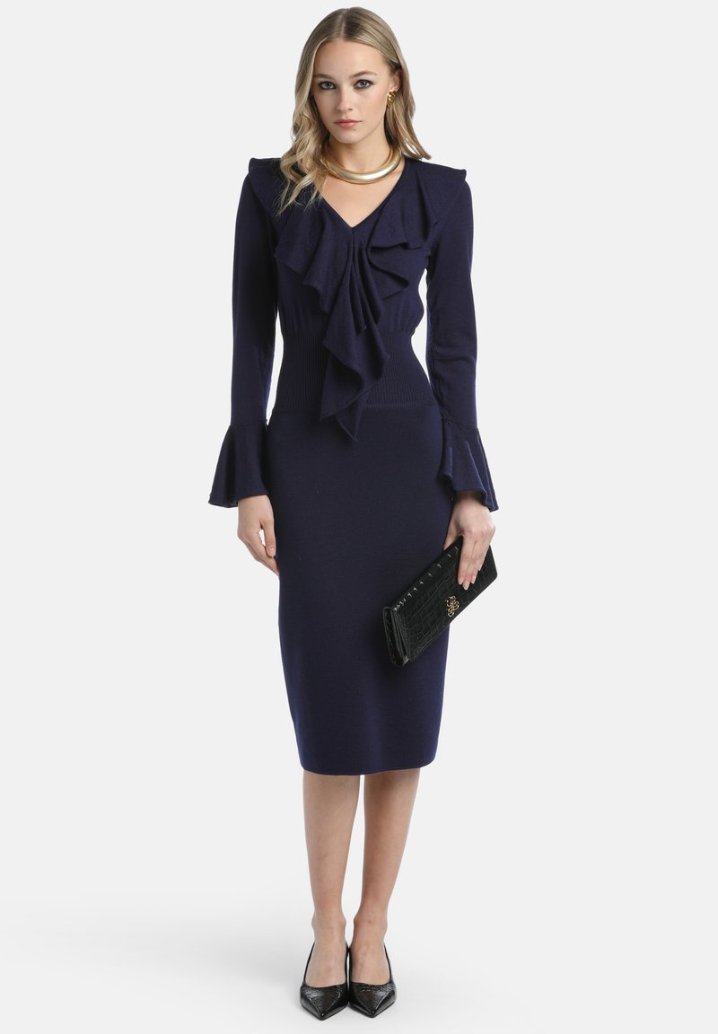 Mornarice oblečena obleka z nabranim ovratnikom in zvončastimi rokavi, narejena iz mehke tkanine. V kombinaciji s črno torbico in čevlji z visoko peto.