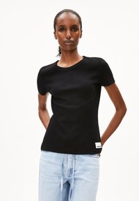 Sort ribbet t-shirt med korte ærmer og rund hals, prydet med et lille hvidt mærke ved bunden. Sammen med lyseblå jeans.