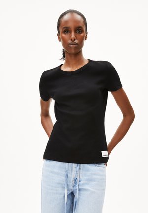 Camiseta negra de manga corta con un cuello redondo, que presenta una pequeña etiqueta blanca en el dobladillo inferior. Combinada con unos jeans de color azul claro.