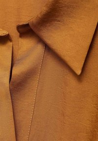 Tela de satén marrón con una textura suave y brillante, que presenta un cuello doblado y detalles de costura vertical, con un tono rico y cálido.