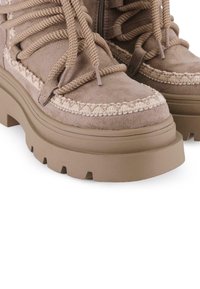 Botas de ante marrón hasta el tobillo con costuras texturizadas y suelas gruesas y estriadas. Incluyen cordones a juego y una cremallera lateral para facilitar su uso.
