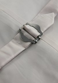 Sangle en tissu gris sécurisée par une boucle métallique argentée décorative sur un fond textile gris clair lisse.