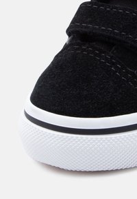 Κοντινή λήψη μαύρου σουέντ αθλητικού παπουτσιού με λευκή ελαστική σόλα, που διαθέτει υφή για καλύτερο κράτημα και αντίθετη μαύρη ρίγα κατά μήκος της άκρης.