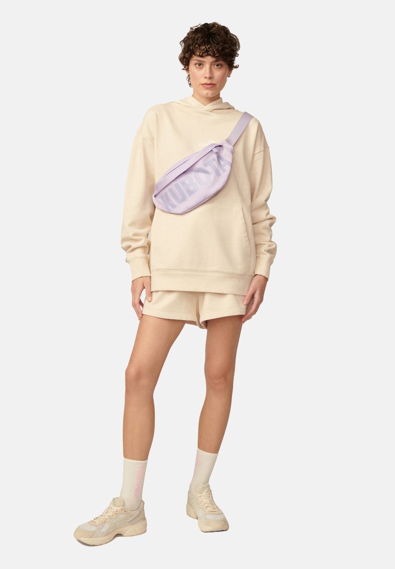 Beżowy, oversize'owy hoodie, dopasowane szorty i jasne sneakersy. Lawendowa nerka z napisem "KUBOTA" na przodzie. Miękka tkanina, casualowy styl.
