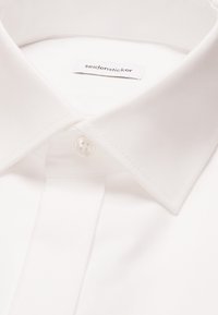 Col de chemise blanche avec un seul bouton fermé et une étiquette visible "seidensticker" à l'intérieur du col.