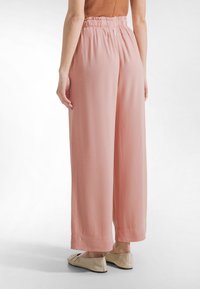 Ljusrosa byxor med vida ben, tillverkade av mjukt, lätt tyg med resår i midjan. Slät textur, utan synliga mönster eller detaljer.