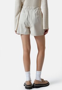 Pantaloni corti in cotone crema con vita elasticizzata, taglio dritto e due tasche posteriori, abbinati a calzini bianchi e scarpe chunky.