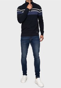 Námořnický svetr s půl zipem, zdobený horizontálními pruhy v světle modré a bílé barvě. Kombinovaný s modrými slim-fit džíny a bílými teniskami.