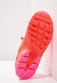 Podešev tenisky Nike v jasné korálové barvě s růžovými akcenty. Obsahuje texturovanou pryž s mřížkovým vzorem a logo "Nike Air" na straně.