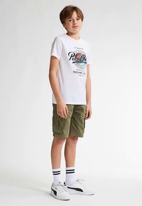 Weißes T-Shirt mit einem farbenfrohen Miami-Logo, olivgrüne Cargo-Shorts, weiße Turnschuhe mit schwarzen Akzenten und weiße Socken mit schwarzen Streifen.