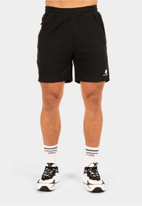 Zwarte atletische shorts met een elastische tailleband, zijzakken en een gestructureerde stof. Opvallende witte logo aan de onderkant links.