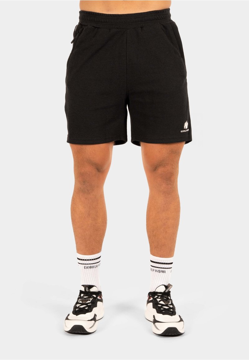 Zwarte atletische shorts met een elastische tailleband, zijzakken en een gestructureerde stof. Opvallende witte logo aan de onderkant links.