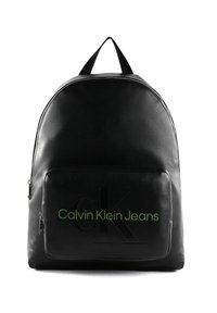 Zaino in pelle nera dalla forma arrotondata, tasca frontale con zip, logo 'CK' in rilievo e testo 'Calvin Klein Jeans' in verde. Manico superiore per il trasporto.