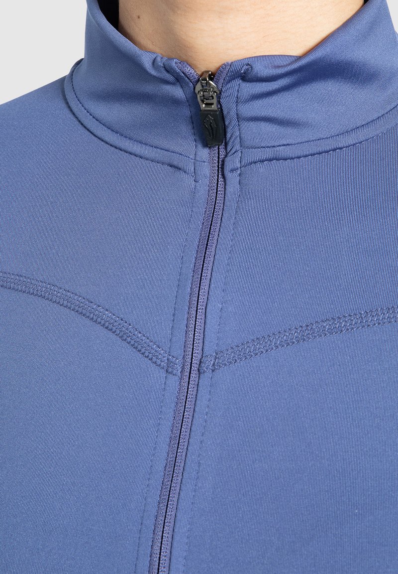 Prenda de abrigo con cremallera en una tela suave y estructurada. Presenta un cuello alto, textura suave y acentos de costura horizontal en un color azul apagado.