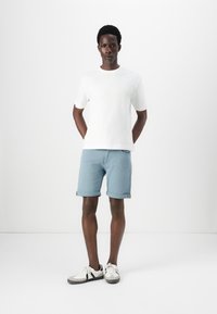 Lys blå denimshorts med opsmøgte bukseben, sammen med en almindelig hvid t-shirt med rund hals og hvide sneakers med grå detaljer.