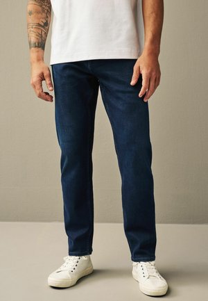 Dark blue denim jeans with a straight cut, slightly faded texture, paired with white low-top sneakers on a neutral background.