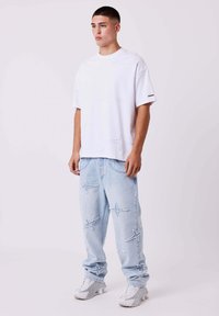 Witte oversized T-shirt met subtiele sterrenpatronen, gecombineerd met lichtblauwe jeans met stervormige uitsparingen en witte sneakers.