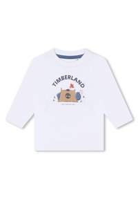 T-shirt bianca a maniche lunghe con stampa grafica "TIMBERLAND", una scena di campeggio e elementi cartooneschi colorati. Chiusura a scatto sulla spalla.