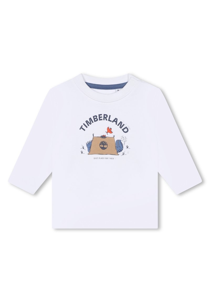T-shirt bianca a maniche lunghe con stampa grafica "TIMBERLAND", una scena di campeggio e elementi cartooneschi colorati. Chiusura a scatto sulla spalla.