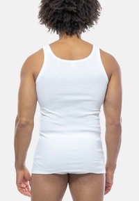 Hvid bomulds tanktop med tætsiddende design, rund halsudskæring og brede skulderstropper, vist fra ryggen.