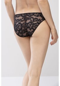Bikini in pizzo nero con motivo floreale, tessuto trasparente, ampia cintura elastica e bordi lisci. Vista posteriore che mostra la copertura e i dettagli del design.
