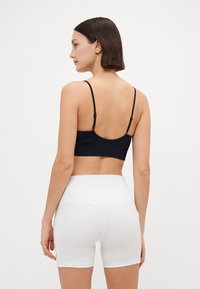 Black sports bra with thin straps, paired with high-waisted white shorts, showcasing a smooth material and fitted design.