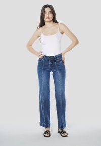 Blauwe denim wijde broekspijpen met een hoge taille, voorzien van een knoopsluiting, voorzakken en zichtbare naaddetails. Gecombineerd met zwarte sandalen.