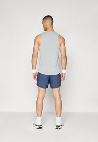 Grauer ärmelloser Tank-Top, marineblaue Shorts, weiße Handgelenkbänder und helle Sportschuhe mit neonfarbenen Akzenten, von hinten betrachtet.