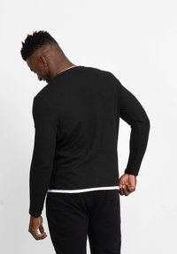 Maglietta nera a maniche lunghe con girocollo a V, caratterizzata da un accento bianco sul colletto e una silhouette aderente. Tessuto strutturato e design semplice.