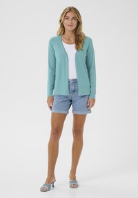 Cardigan côtelé bleu clair, t-shirt blanc ajusté, shorts en denim roulés et sandales à talons bleu clair. Design simple sans motifs.