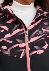 Black and pink zip-up jacket featuring a brushstroke pattern, soft fabric, high collar, and logo detail on the chest.