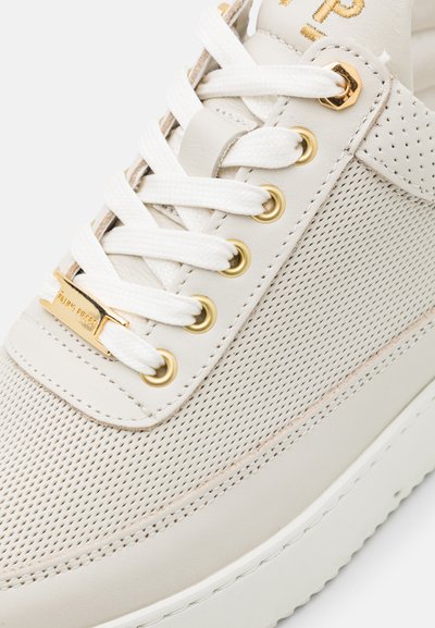 Weißer perforierter Ledersneaker mit goldenen Details, weißen Schnürsenkeln und einer strukturierten Sohle. Er zeichnet sich durch ein elegantes Design und minimalistische Markenkennzeichnung aus.