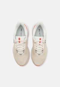 Beige treningssko med mesh-overdel, hvit såle og oransje detaljer. Har snøring, logo-akenter og en polstret såledesign.