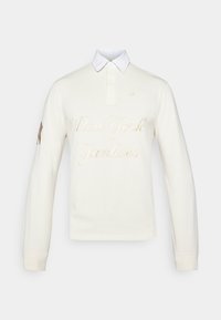 Long-sleeve polo shirt in cream with white collar, featuring "New York Yankees" in gold embroidery and logo detail on the sleeve.