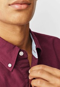 Bordeaux overhemd met knopen en een contrasterende lichtblauwe patroonkraag, voorzien van witte knopen en een textuur die zichtbaar is bij de hals.