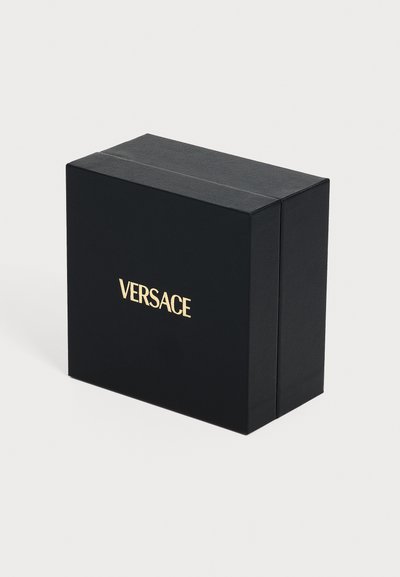 Μαύρο ορθογώνιο κουτί με χρυσό λογότυπο Versace στο κέντρο μπροστά, τοποθετημένο σε απλό ανοιχτό φόντο.