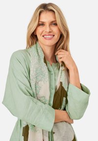 Light green linen shirt with button closure and three-quarter sleeves, paired with a patterned scarf in cream, green, and brown tones.