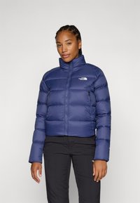 Námornícka puffy bunda s vysokým golierom, zipsom a dvoma bočnými zipsovými vreckami. Obsahuje prešívaný dizajn a logo The North Face na hrudi.
