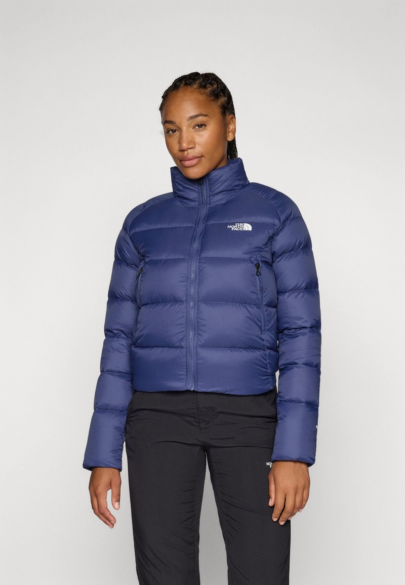 Námornícka puffy bunda s vysokým golierom, zipsom a dvoma bočnými zipsovými vreckami. Obsahuje prešívaný dizajn a logo The North Face na hrudi.