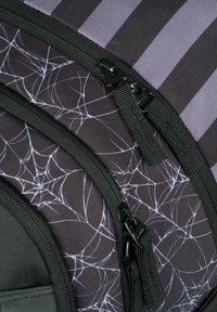 Černý látkový batoh se vzorem pavučiny, několika zipy s černým kováním a vertikálními fialovými pruhy.