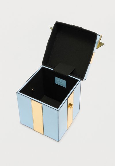 Ορθογώνιο κουτί γαλάζιου και μπεζ χρώματος με ανοιχτό μαύρο εσωτερικό καπάκι που δείχνει ένα μικρό χρυσό κούμπωμα στην πλευρά.