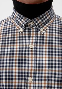 Overhemd met knopen in een blauw, bruin en wit ruitpatroon; voorzien van een kraag en parelknoopjes; stof heeft een gladde textuur.