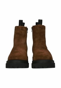 Botines de ante marrón con suela gruesa de goma negra, que cuentan con un cierre de cremallera lateral y una lengüeta en el talón para ponerlos con facilidad.