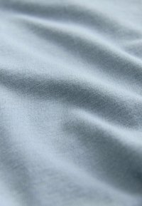 Svijetloplavi pamučni materijal s glatkom teksturom, sa finim rebrastim uzorkom i suptilnim naborima, što ukazuje na fleksibilnost i mekoću.