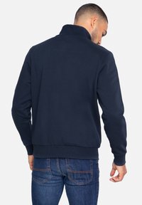 Marineblauw sweatshirt met een hoge kraag, geribde manchetten en zoom, met een gladde textuur en een eenvoudig design. Draagt bij blauwe jeans.
