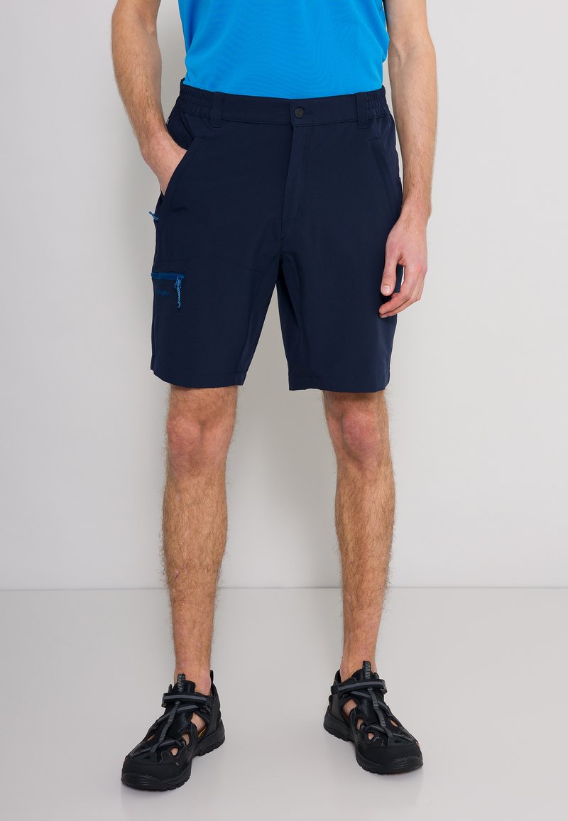 Marinblå shorts i lätt material, med två framfickor och en ficka på sidan med dragkedja i blå nyanser. Bärs med svarta sportskor.