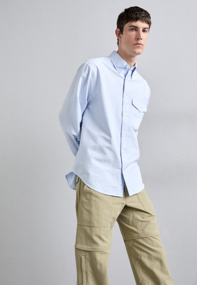 Chemise bleu clair à boutons avec une poche poitrine, assortie à un pantalon cargo beige avec plusieurs poches et des détails de couture.