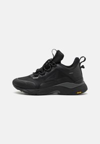 Chaussure de sport noire avec une tige en mesh respirant, une semelle épaisse en caoutchouc, des détails texturés et un logo Vibram bien visible sur la semelle extérieure. Conception imperméable.