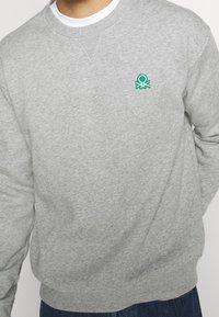 Grå sweatshirt med ribbad rund halsringning. Har en liten grön broderad bläckfiskdesign på vänster bröst. Mjuk bomullsmaterial.